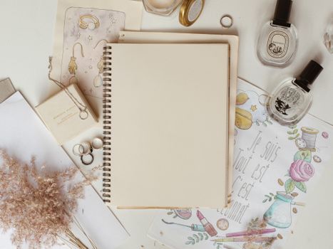 Carnet de stylisme entouré de bijoux, parfums et illustrations sur une table décorative.