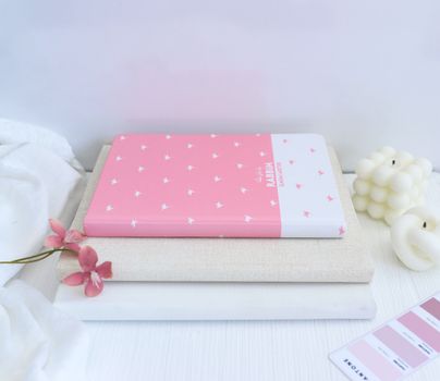 Carnets de stylisme empilés sur une surface blanche, avec une fleur rose et des bougies en arrière-plan.